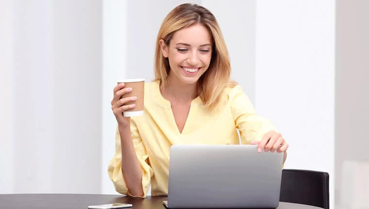 コーヒーを飲みながらPCで作業をしている黄色い服を着た女性